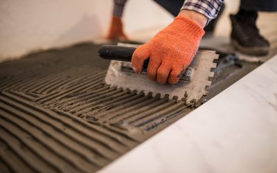 Troweling mortar onto a concrete floor in preparation for laying white floor tile.